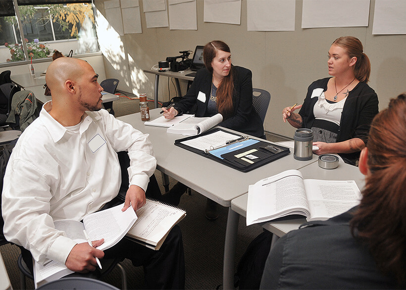 Three students in business attire having a discussion around a table