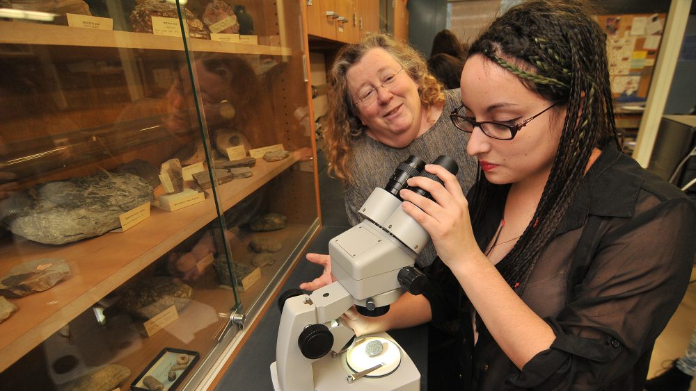 Student looking in microscope with instructor in front of rocks