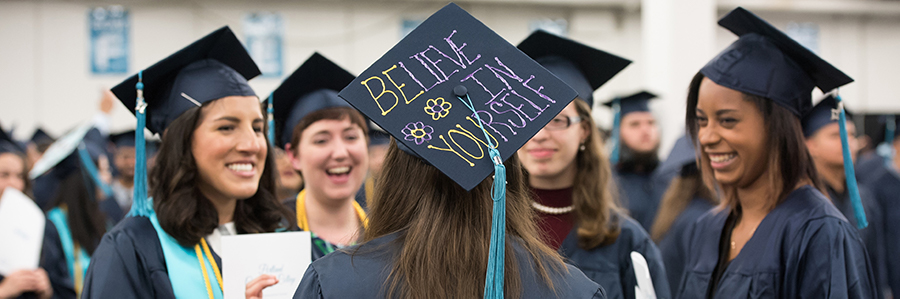 Students at graduation, one of the hats says 'believe in yourself'