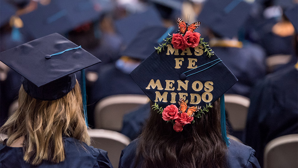 Student with "más fe, menos miedo" written on her graduation cap