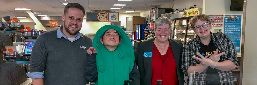 Students, staff, and student in a pickle costume pose near cafeteria